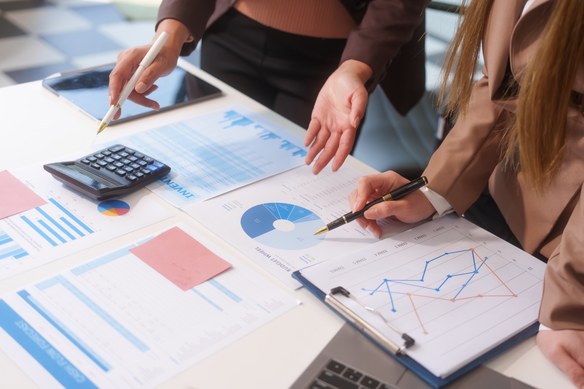 Close-up of two businesswomen working at desk discussing business strategies, analyzing financial